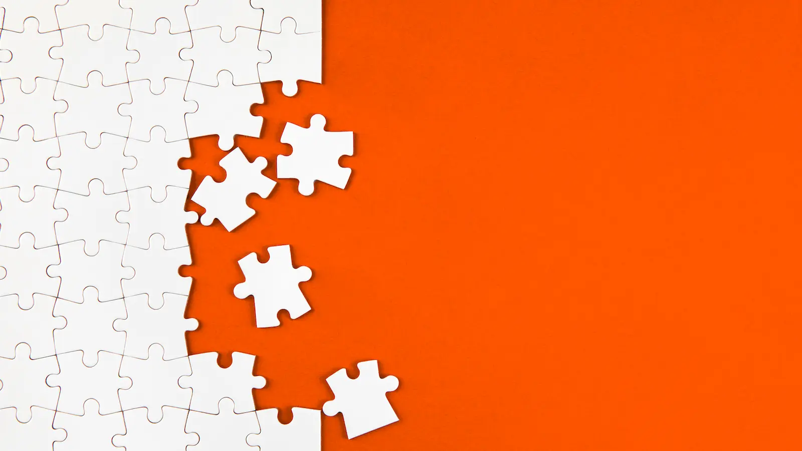 Partially assembled white jigsaw puzzle on an orange background, its edge still taking shape, with a few loose pieces resting beside the assembled section